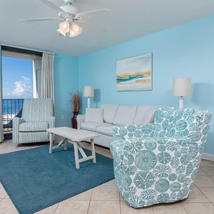 Living area features a cozy sofa with queen sleeper, patterned chairs, and a table, with a view of the beach from the balcony