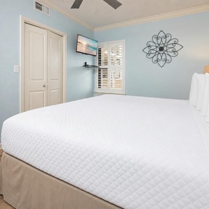 Rest in the comfortable bedroom with a large king bed, soft blue walls, and a TV for entertainment
