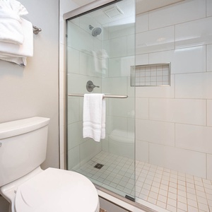 The master bathroom features a sleek walk-in shower with glass doors, fresh white towels, and a refreshing beach vibe