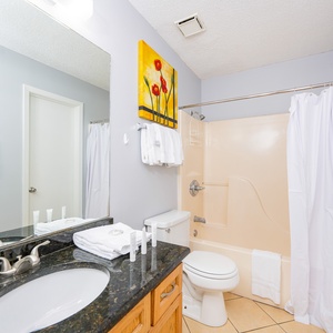 The bathroom features a dark countertop, a tub/shower combo, and fresh towels neatly arranged on the sink
