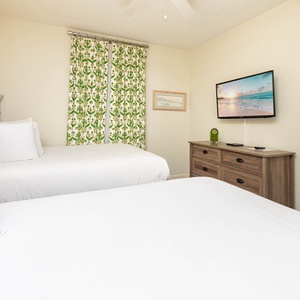 Cheerful guest bedroom with two double beds, vibrant decor, and a TV for entertainment