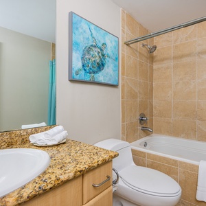 Bright guest bathroom featuring a jetted tub, granite countertops, and a colorful sea turtle painting for a refreshing vibe