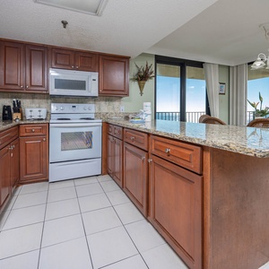 The kitchen features rich wood cabinetry, granite countertops, and a breakfast bar with views of the beach