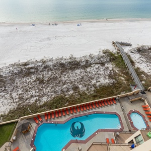 The image showcases the vibrant pool area with orange lounge chairs and a view of the beach and white sand beyond