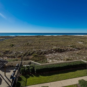 Expansive view of the beach with glistening waters, framed by lush greenery and a wooden walkway leading to the shore