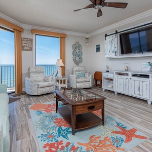 Cozy living area features a light blue sofa with queen sleeper, two chairs, and a beach view through balcony doors