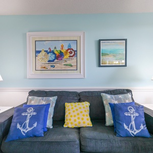 The cozy living area features a gray sofa adorned with colorful pillows, complemented by beach-themed artwork and lamps