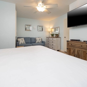 The master features a king bed, a blue sofa, and a mounted TV, complemented by soft lighting and beach decor