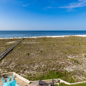 A boardwalk leads you across coastal dunes toward the calm water and colorful umbrellas dotting the beach front