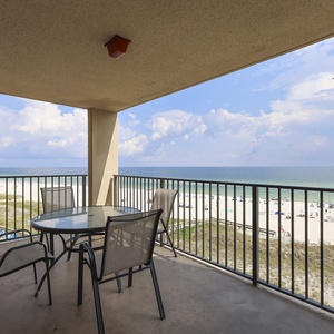 The balcony features a round table with four chairs, offering a captivating view of the beach and tranquil waters