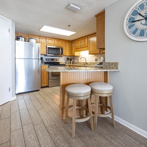 The modern kitchen features wood cabinetry, a breakfast bar with two stools, and a sleek granite countertop