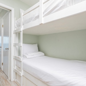 This cozy bunk area features fresh white bedding and a light green wall, perfect for kids to relax after beach adventures