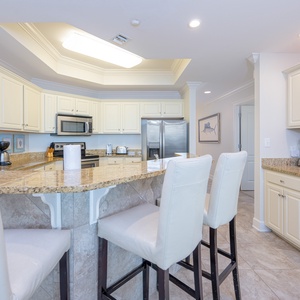 Kitchen featuring sleek stainless appliances and a spacious granite countertop with stylish white bar stools
