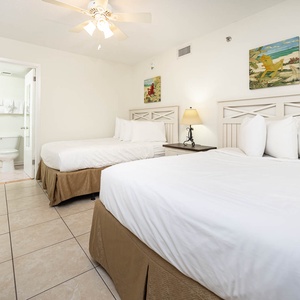 Bright and airy guest bedroom featuring two comfortable double beds, a bedside lamp, and easy access to an adjoining bathroom