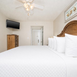 This cozy bedroom features a wooden headboard, a TV for entertainment, and a serene atmosphere for restful nights
