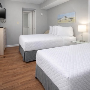 The guest room features two double beds, a stylish lamp, and a TV, perfect for a relaxing stay