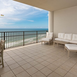 This tenth-floor balcony features comfortable white seating and a dining table, overlooking the beach and pool area