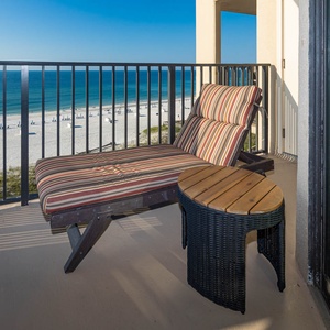 A striped lounge chair and small table offer a relaxing spot on the balcony with a beautiful view of the beach and water