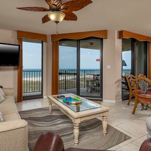 Living area features a comfortable sofa with queen sleeper, a glass coffee table, and a dining area with beach views
