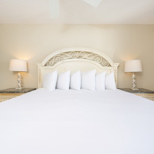 A beautifully styled master suite features a large bed with crisp white linens, with elegant lamps on ornate nightstands