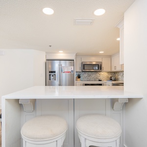 This kitchen features a marbled breakfast bar with two stools, sleek cabinetry, and modern stainless appliances