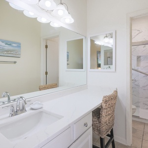 Bright master bath featuring a sleek marble countertop, modern lighting, and a walk-in shower, complemented by woven seating