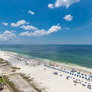 A panoramic view showcases the vibrant beach with colorful umbrellas and sunbathers against a backdrop of clear blue skies
