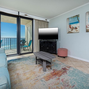 This inviting living area features a large TV, queen sofa-sleeper, colorful decor, and a balcony with a beautiful beach view