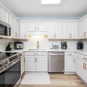 White cabinetry and elegant gold accents in this kitchen with a sleek countertop, Keurig, coffee maker, and backsplash