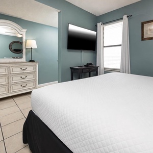 This bedroom features a comfortable bed, a large TV, and charming decor with a soothing blue wall color