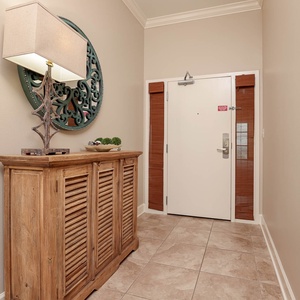 The entryway features a stylish wooden console, decorative lamp, and a vibrant wall mirror, setting a warm tone for your stay