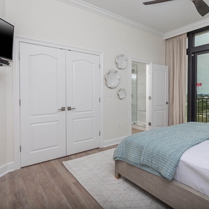 This bedroom features a cozy king bed with a soft blue throw and a mounted TV, offering a lovely view from the large windows