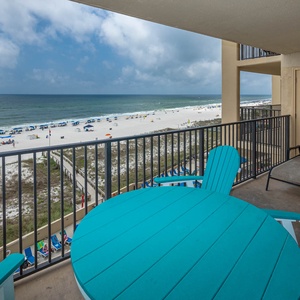 A vibrant turquoise table and chairs on the balcony overlook the beach, inviting relaxation with a stunning coastal view