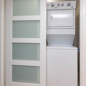 This laundry area features a stacked washer and dryer behind a sleek, frosted glass door for your convenience