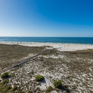 Expansive view of the beach with white sand and turquoise waters, framed by the dunes and a wooden boardwalk access