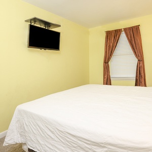 Cozy guest space featuring a queen bed, a mounted TV, and elegant drapes framing the window