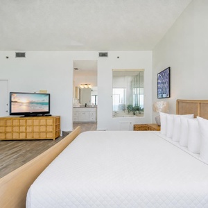 Relaxing master bedroom featuring a king bed, modern TV, and an inviting view through the adjoining bathroom