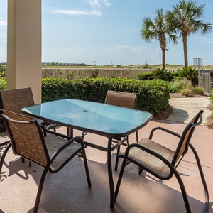Outdoor patio area featuring a glass table and four chairs, surrounded by lush greenery and palm trees, inviting relaxation