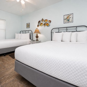 This guest bedroom features two metal-framed queen beds with plush white bedding, complemented by coastal-themed wall art
