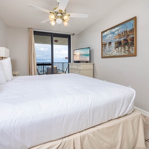Master bedroom featuring a king bed, a TV, and access to a balcony with a view of the gulf beyond