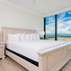 Serene guest bedroom featuring a large king bed, fluffy pillows, and expansive windows showcasing beautiful views