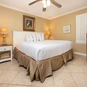 The cozy bedroom features a king bed with decorative pillows, a bedside lamp, and a flat-screen TV mounted on the wall