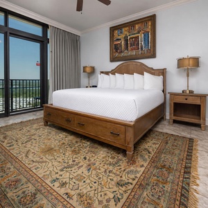 The master bedroom features a cozy atmosphere with a plush king bed, a stylish area rug, and balcony access with a beach view