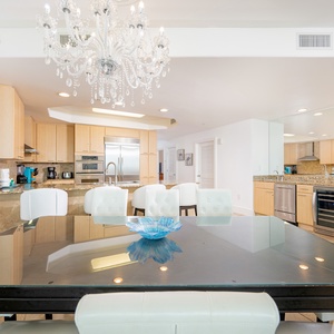 Elegant dining area with a glass table, eight white chairs, and a view of the spacious and modern kitchen