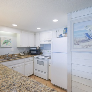 This kitchen features white cabinetry, granite countertops, and a beach-themed artwork, perfect for culinary adventures