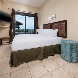 Brightly decorated master bedroom features a king bed, a mounted TV, leading to the outdoor beach patio
