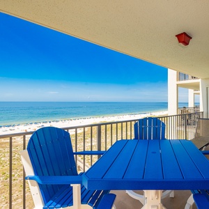 Balcony features a blue table and chairs with a view of the beach and gulf, inviting relaxation under a clear sky