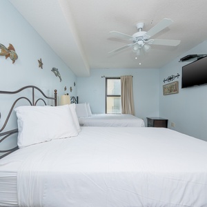 Bright guest room features two queen beds with white linens, a ceiling fan, and wall decor of fish and stars, plus a TV