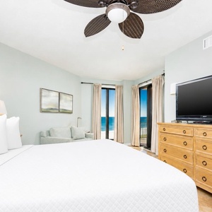 The master bedroom features a king-sized bed, a large TV, and stunning beachfront views through sliding glass doors