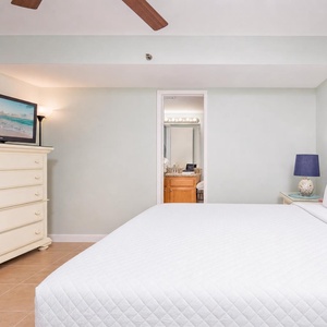 Bright and inviting bedroom featuring a plush king bed and a flat-screen TV, with a glimpse of the stylish bathroom